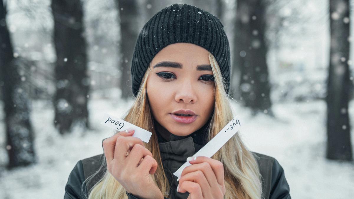 woman in black knit cap and gray jacket holding white printer paper