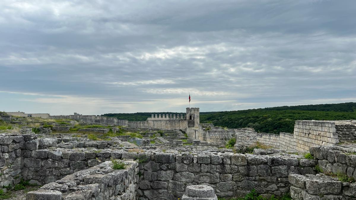 a stone wall with a stone wall and grass and a cloudy sky