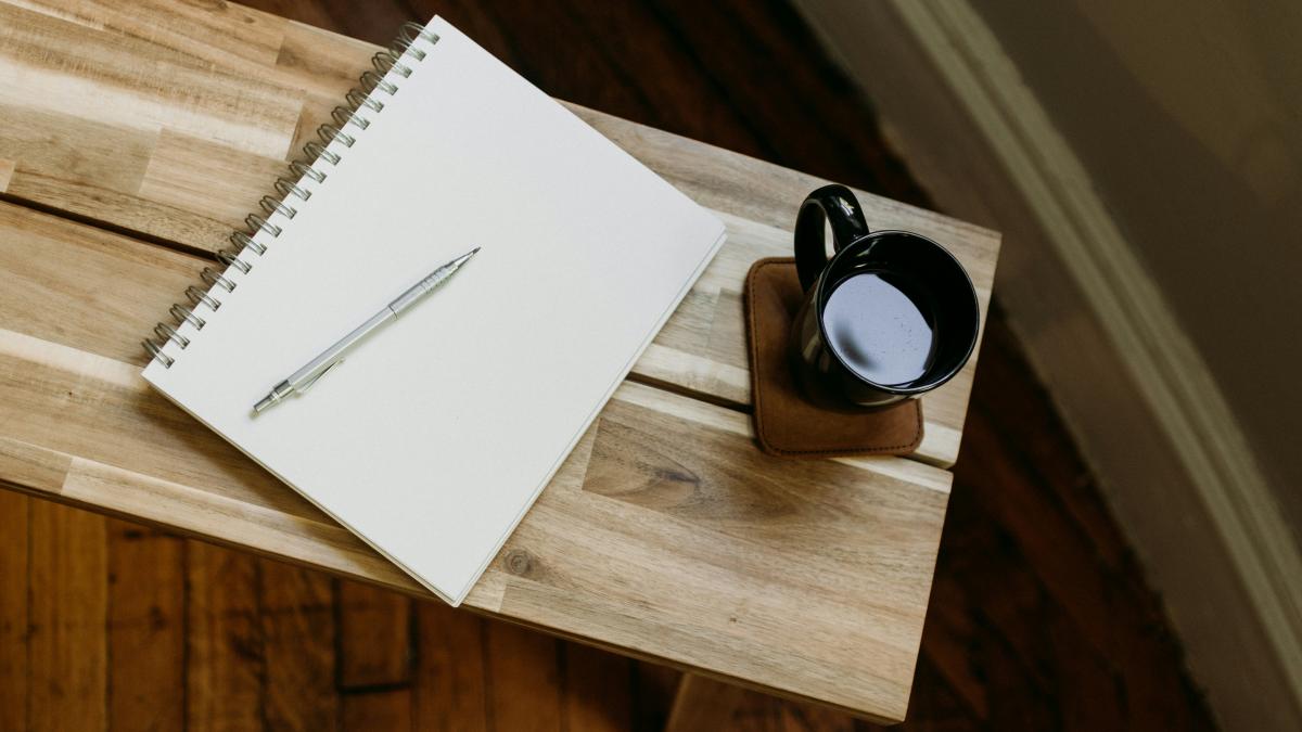 a cup of coffee and a pen on a wooden table