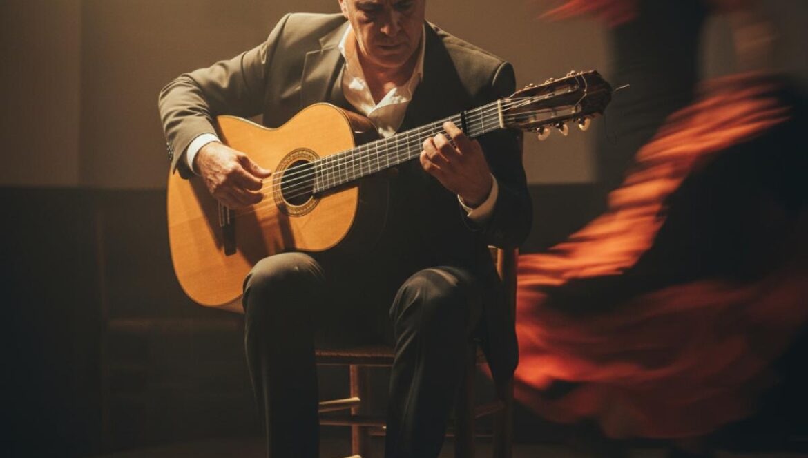 Guitariste flamenco sur une petite scène, éclairage chaud, danseuse floue en arrière-plan.