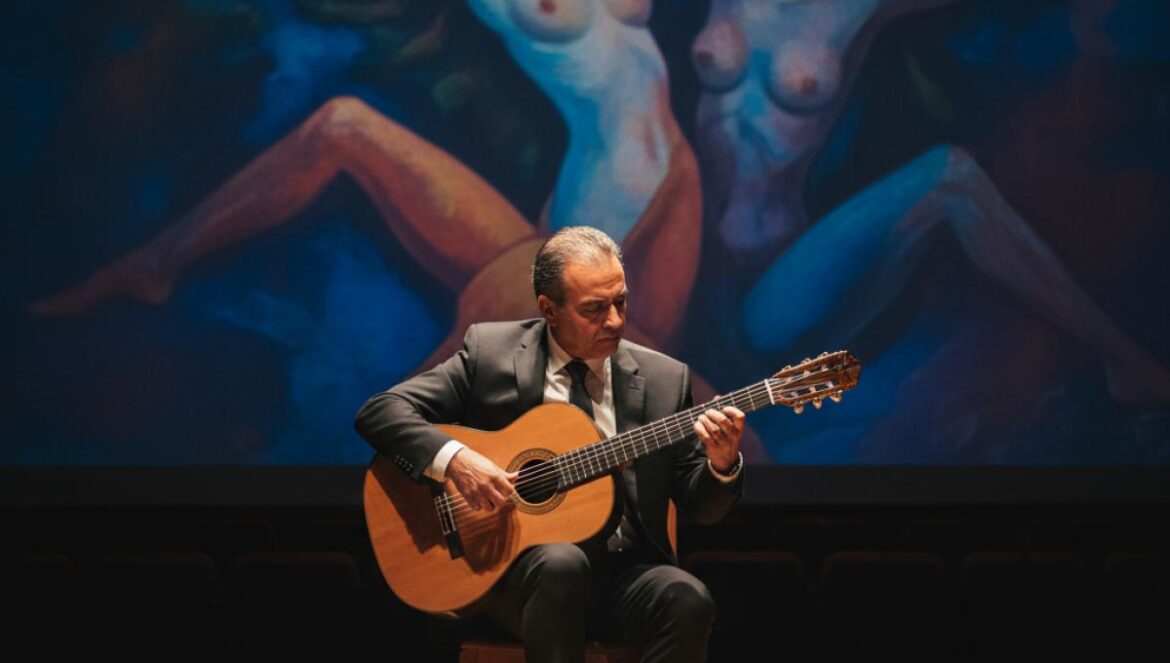 Un guitariste classique joue sur scène, devant la projection floue d’une peinture andalouse évoquant l’univers de Romero de Torres.