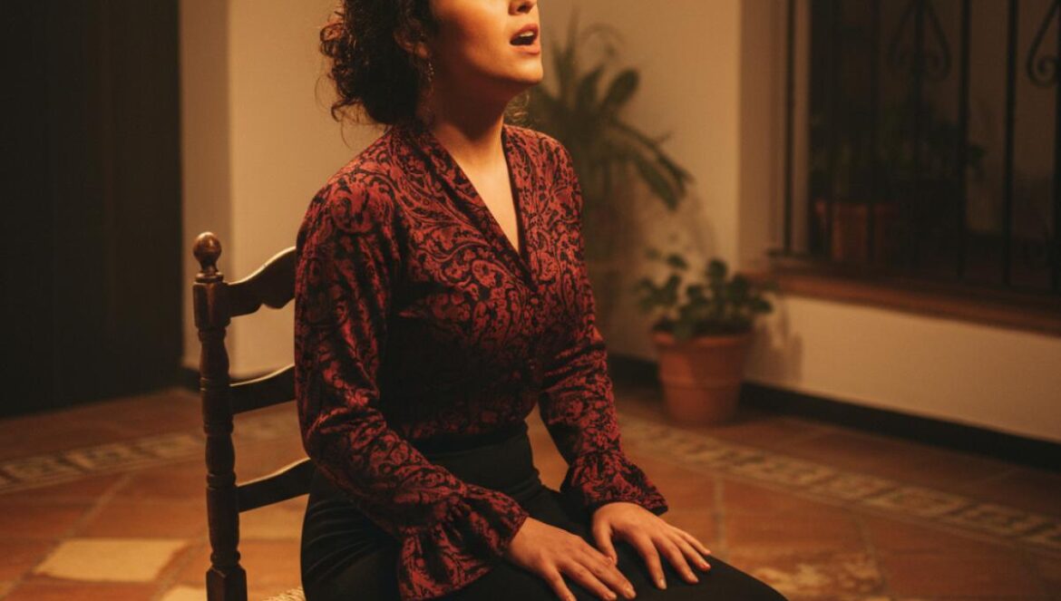 Chanteuse de flamenco en répétition sur une petite scène andalouse, lumière chaude, chaise en bois et azulejos en arrière-plan